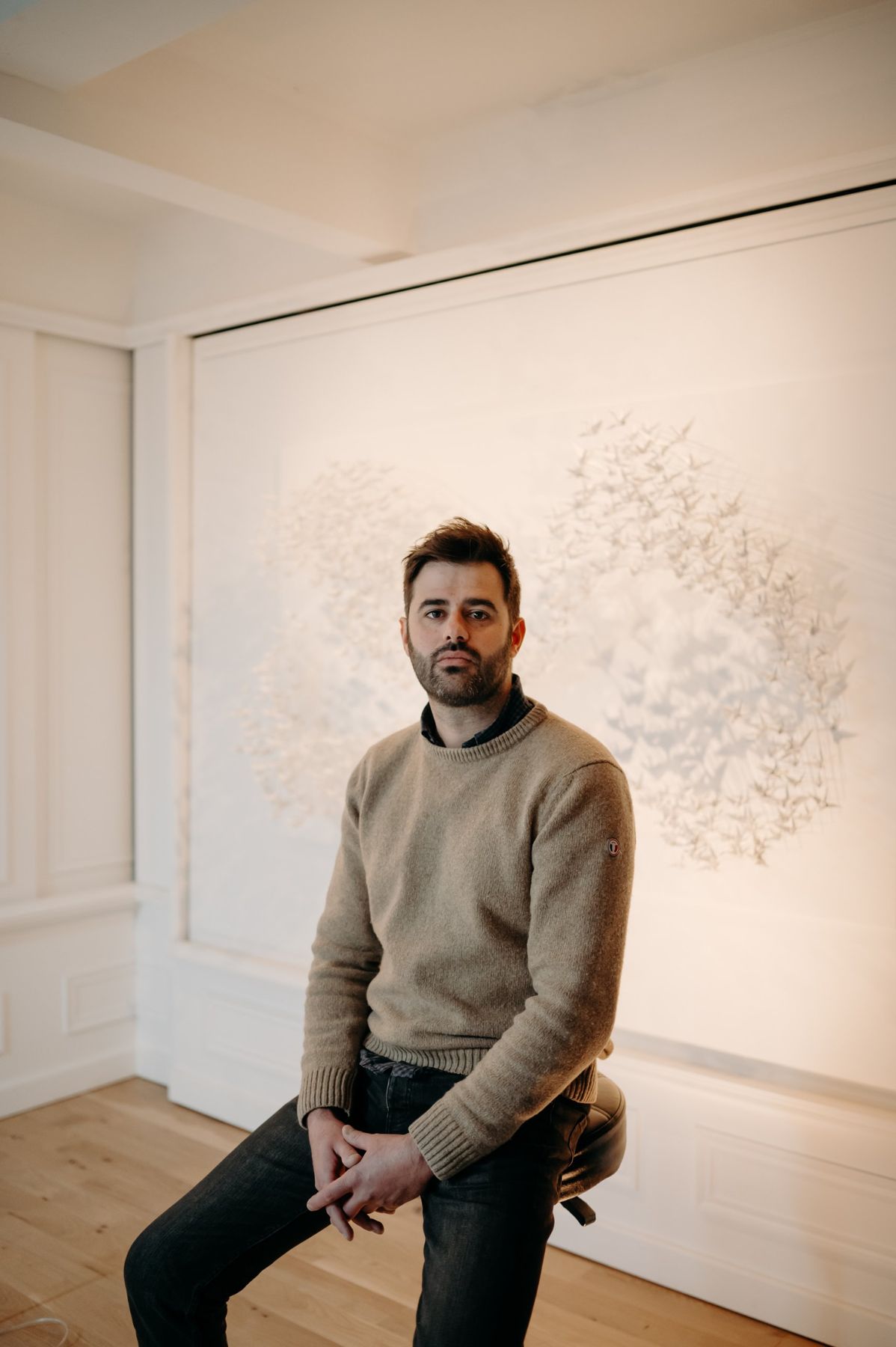 Benjamin Gaumard, assis de trois-quarts devant une Murmuration en papier.
